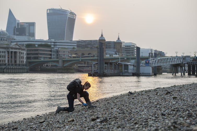 Secrets and techniques of the Thames: mudlarking treasures show off historical past of London’s river and the individuals who scour its banks 1 A mudlark kneels on a rocky shore collecting objects.