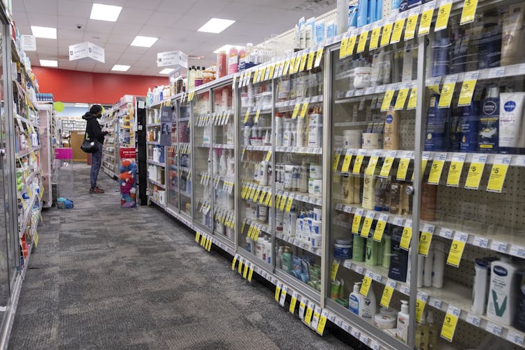 Person in distance shopping in pharmacy aisle with glass-covered cases
