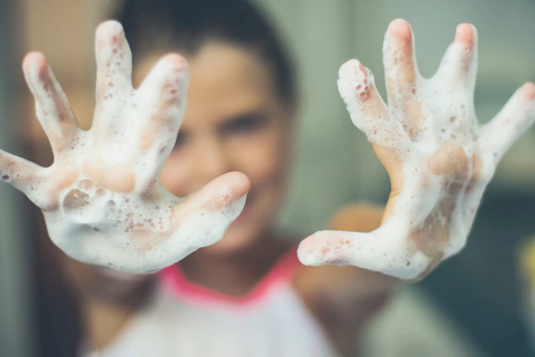 Uma menina estende as mãos ensaboadas em direção à câmera.