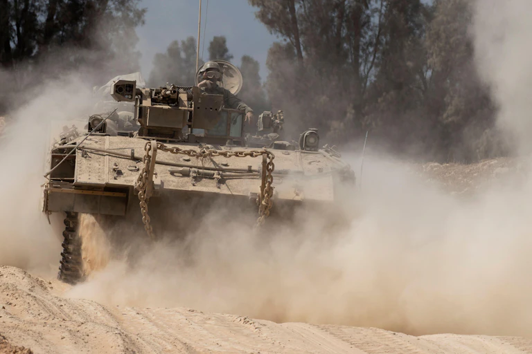 An IDF armoured personnel carrier churning up dust as it prepares to cross into Gaza, May 6 2025.