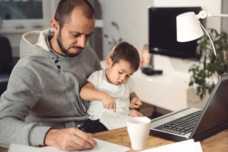 Un homme travaille sur son ordinateur en tenant son enfant