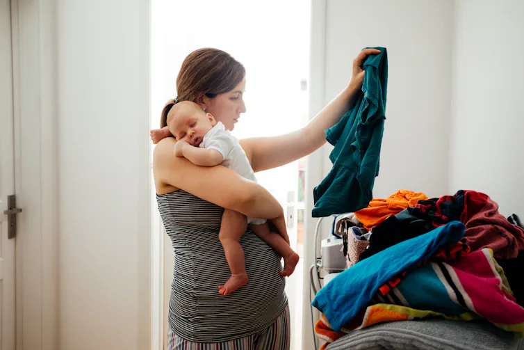 Une femme tient son poupon dans une main, puis plie du linge de l’autre
