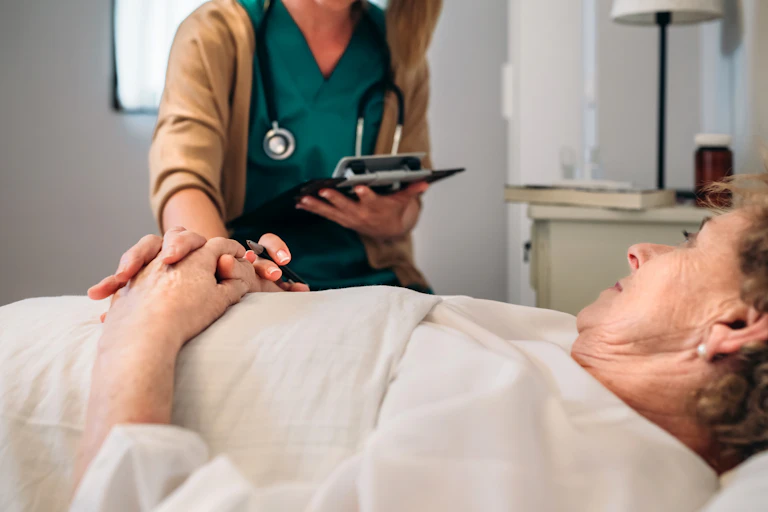 A doctor in green scrubs holds the hand of an older woman patient