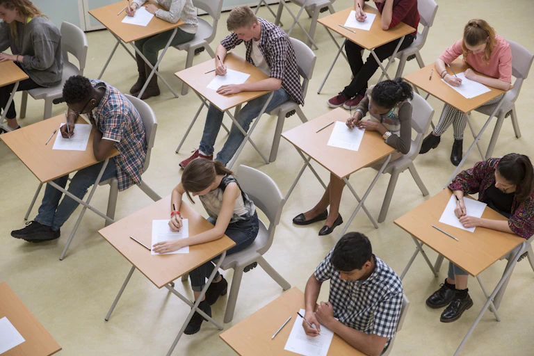 many students sit at wooden desks with their heads down taking tests