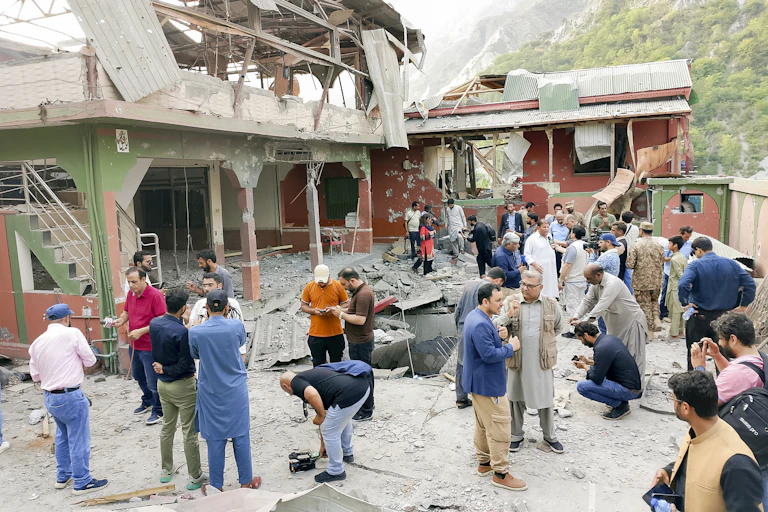 A building lies in ruins while people mill around outside.