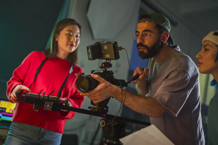 A man holds a camera while a woman beside him assists and another looks on