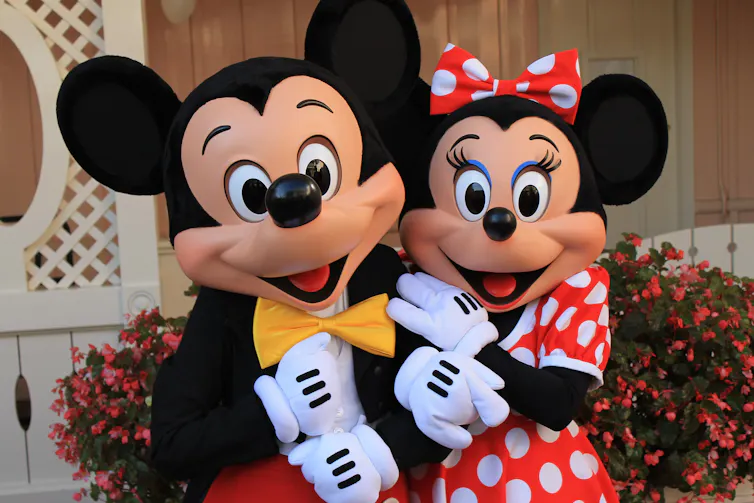 Dress-up mascots of Mickey Mouse and Minnie Mouse. Mickey has no eyelashes and Minnie has long ones.