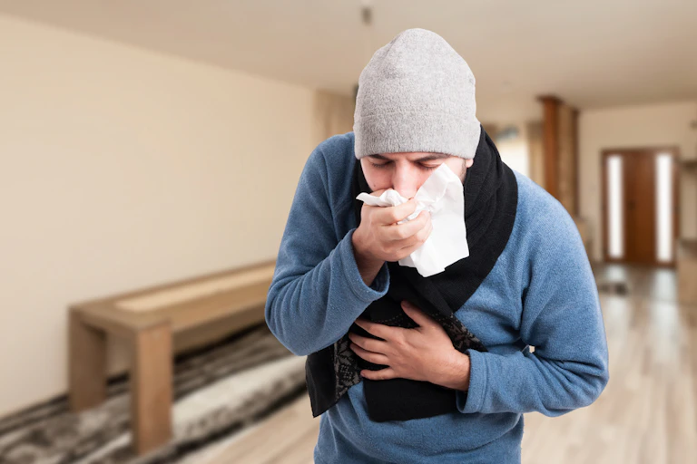 Man wearing beanie and scarf coughing up into tissue