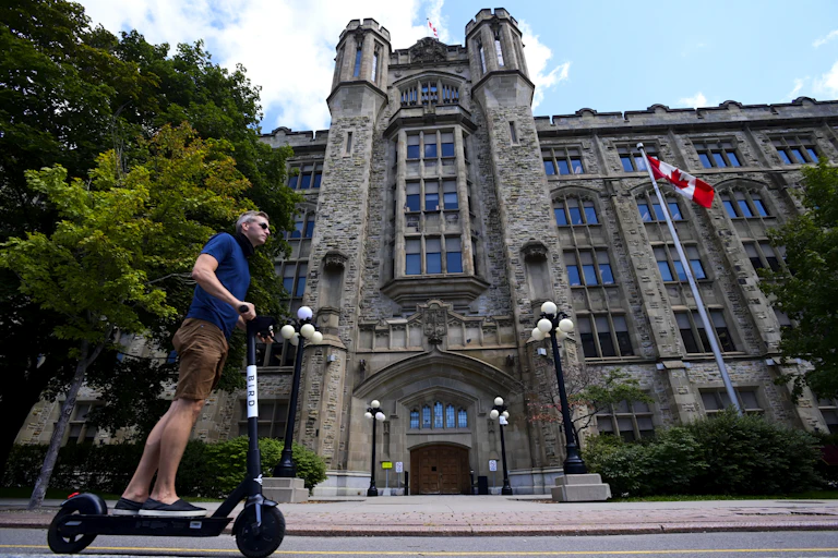 A man on a Segway rides past a stone building with a Canadian flag flying in front of it.