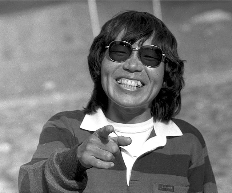 Woman in sunglasses smiling and pointing at the camera.