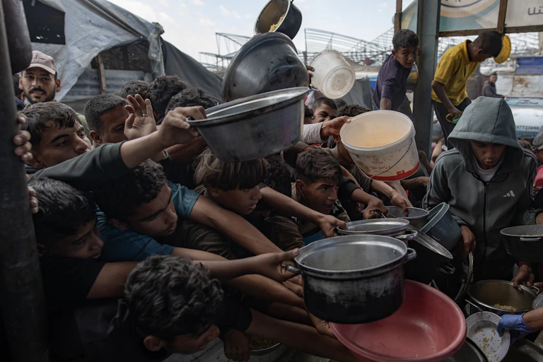 Palestinians push themselves in line to receive a portion of food from a charity kitchen.