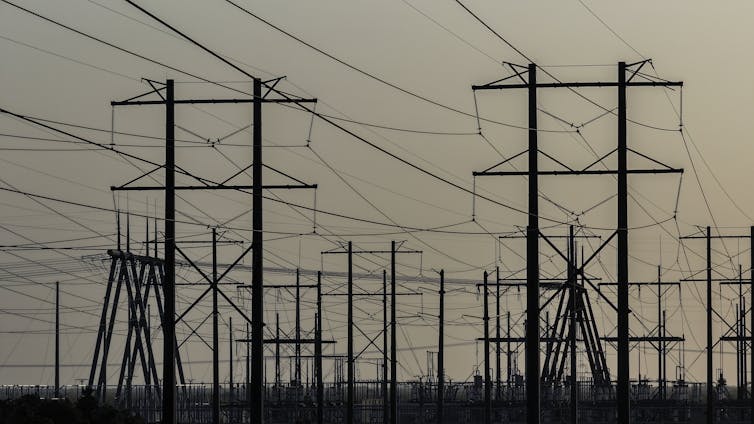 High-voltage power lines run along an electrical power grid shown with overcast sky