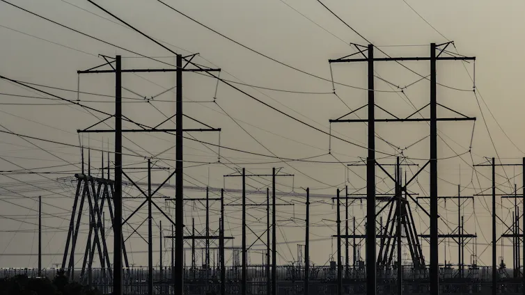 High-voltage power lines run along an electrical power grid shown with overcast sky