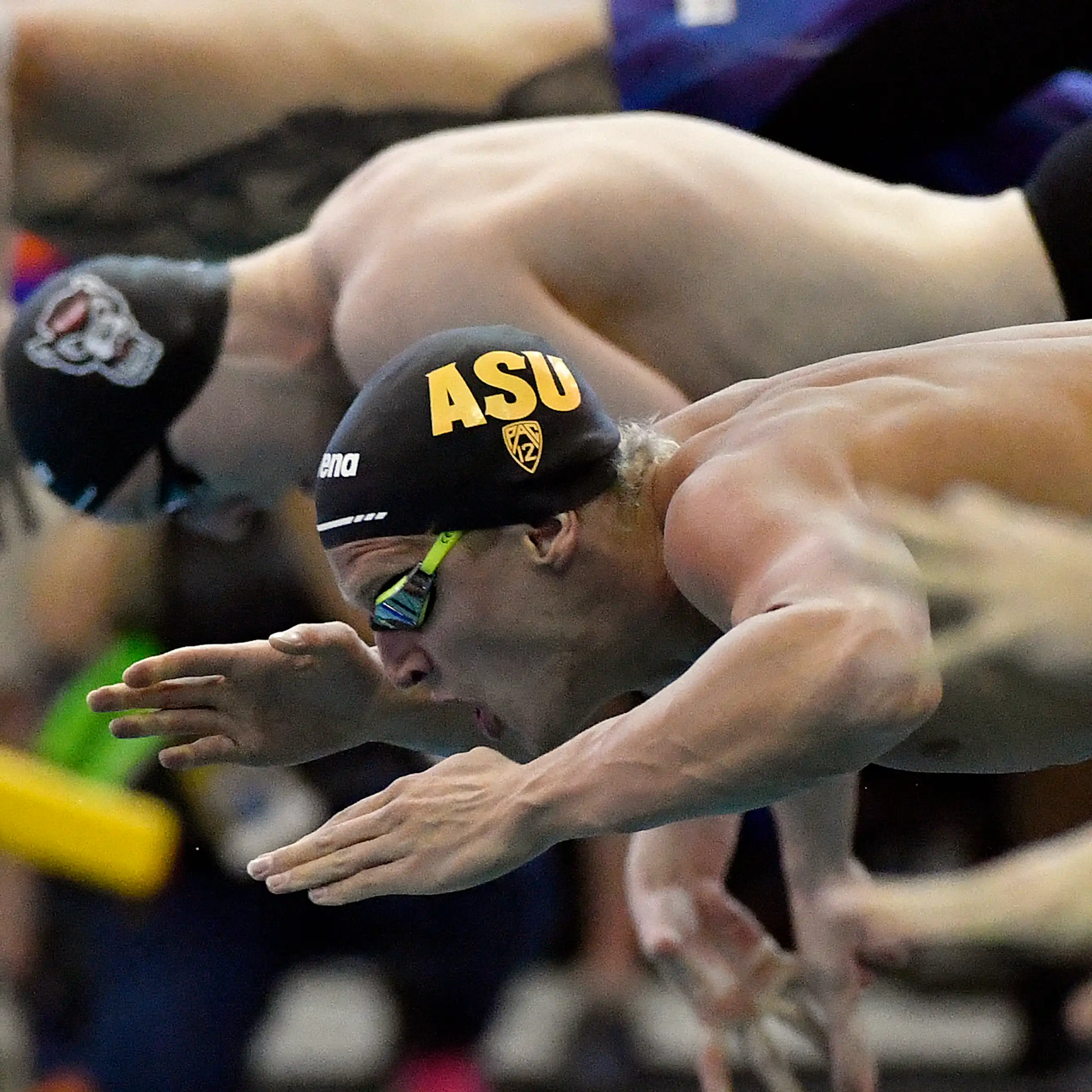 Three swimmers dive into the water at the start of a race.