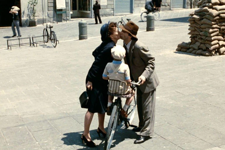 Una pareja se da un beso sobre una bicicleta en la que está un niño.