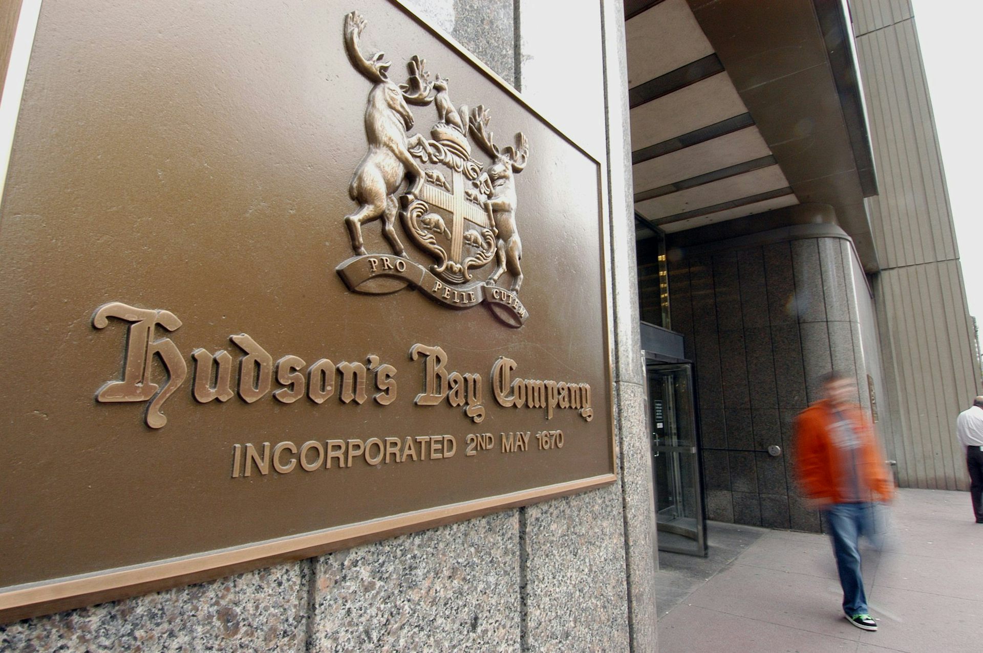 Placa con dos malos en ambos lados de la joroba en el costado del edificio mientras pasa una persona.