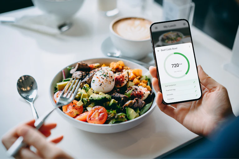 Hand using fitness plan mobile app on smartphone to check the nutrition facts and calories intake of a beef cobb salad.