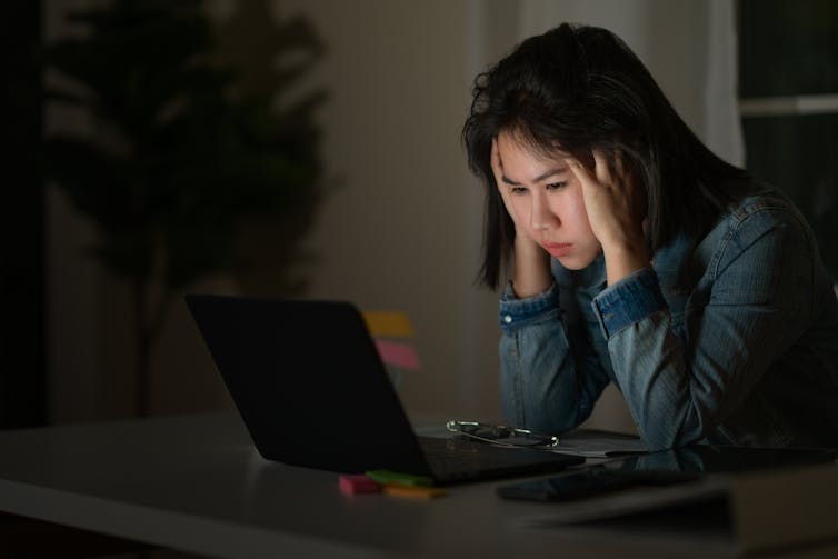 A young woman sits on a laptop with her head
