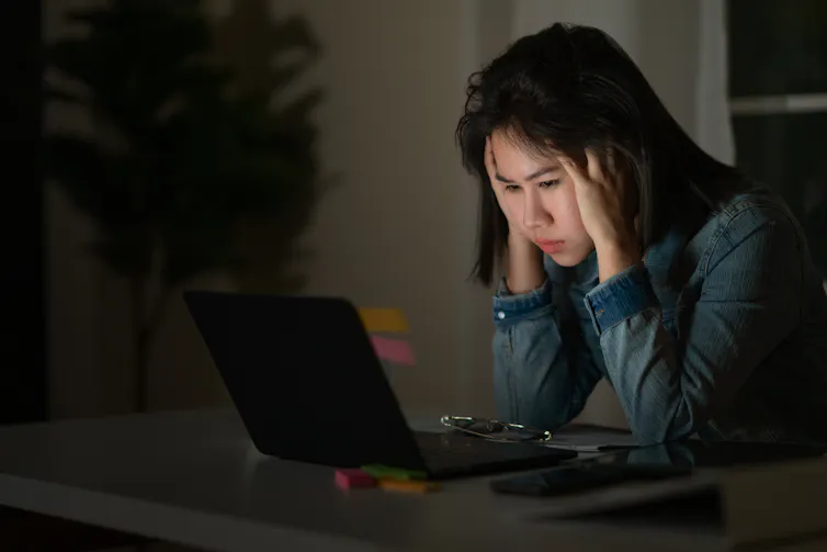 A young woman sitting at a laptop with her head in her hands