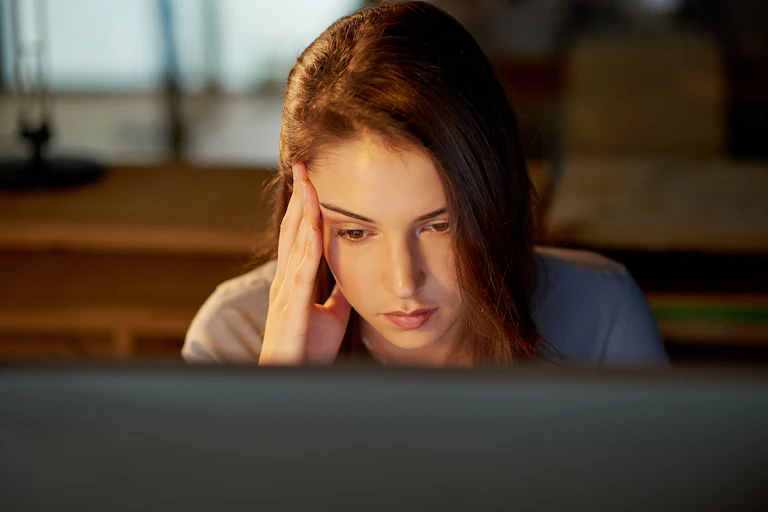 A tired looking woman looks at a computer screen