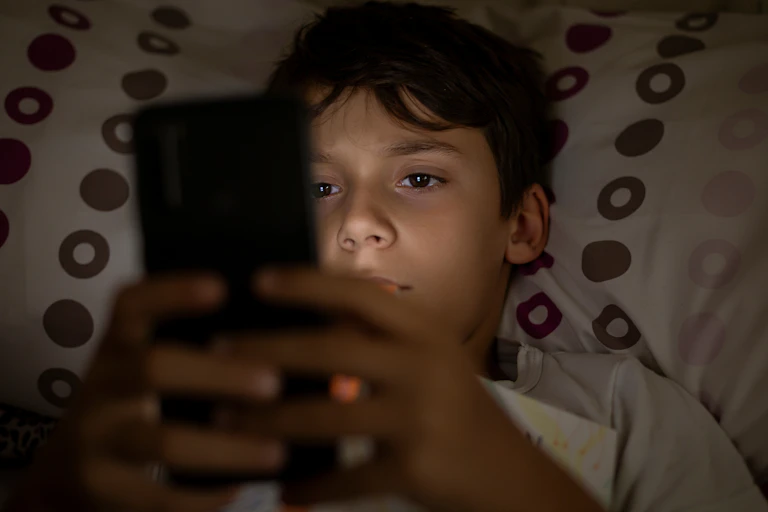 A child lying in bed and using their phone.