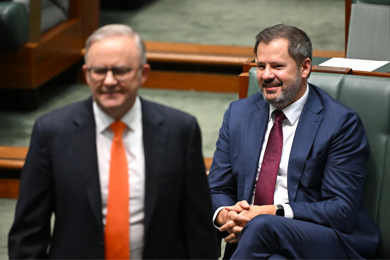 Anthony Albanese walking away from Ed Husic, who's sitting behind him