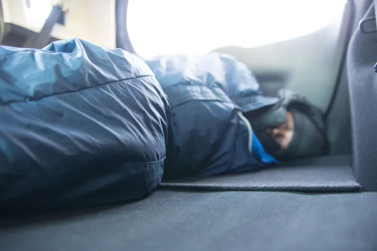 A man sleeps in a sleeping bag inside a car.