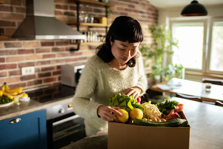 A woman unpacks a box of fresh produce.