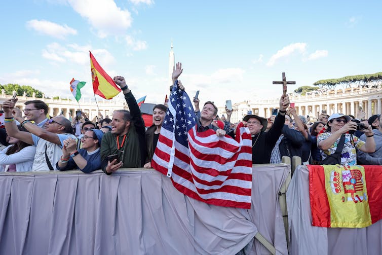 Pessoas agitando uma bandeira dos EUA na praça de São Pedro, em Roma.