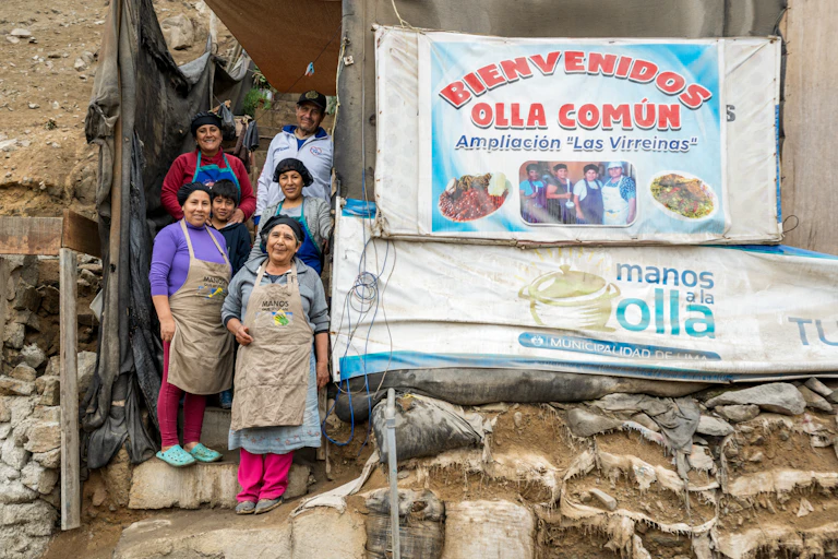 Mujeres posando junto a un cartel en el que da la bienvenida a un restaurante solidario.
