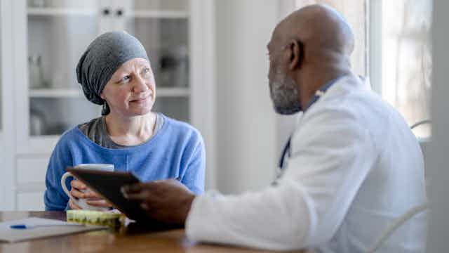 A Black male doctor sits with white woman at a table during a homecare visit.