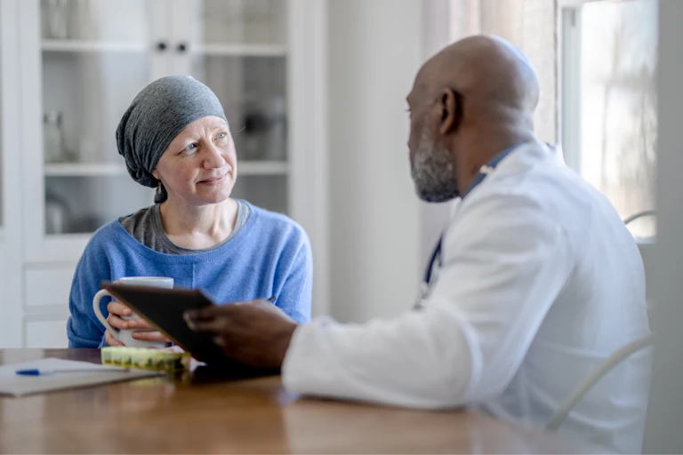 A Black male doctor sits with white woman at a table during a homecare visit.