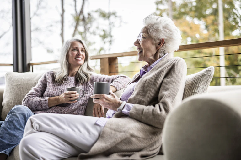 A older woman and her daughter sit on an outdoor patio talking.