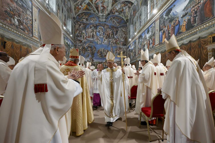 A man in white robes passes through a sea of other men similarly dressed.