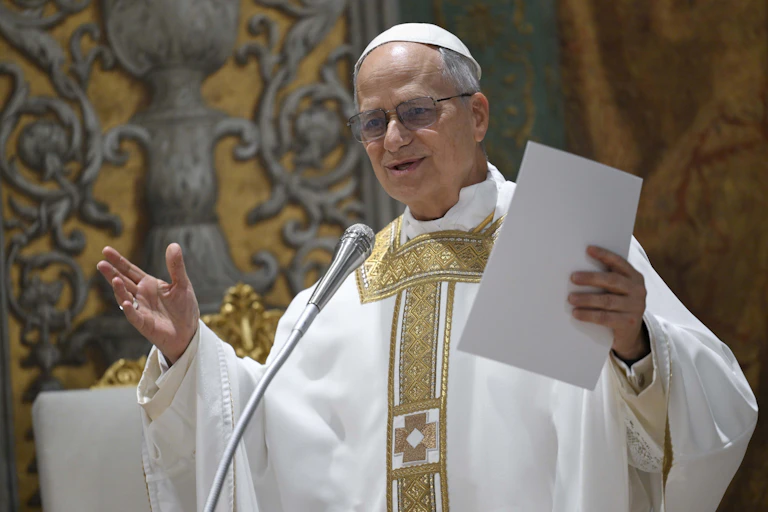 A man in white robes and a white scullcap at a microphone.