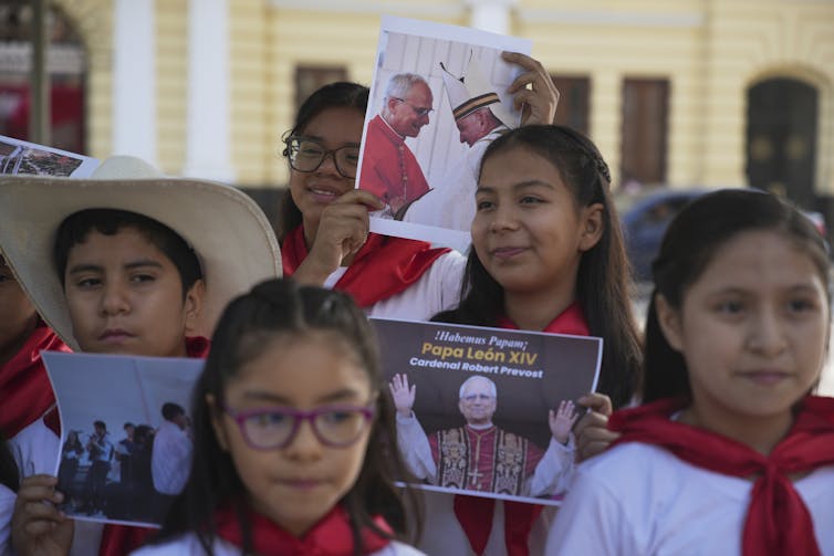 Children outdoors in robes, one holding a photo of a man in a robe.