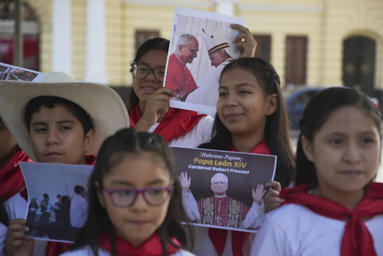 Children outdoors in robes, one holding a photo of a man in a robe.