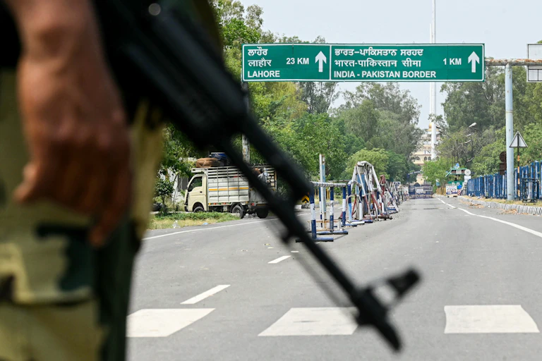 A man with a gun is seen in front of a road sign saying 'India-Pakistan border'
