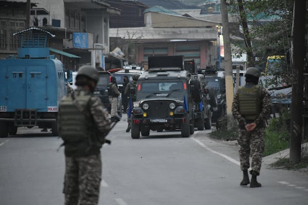 People in army uniforms patrol a street.