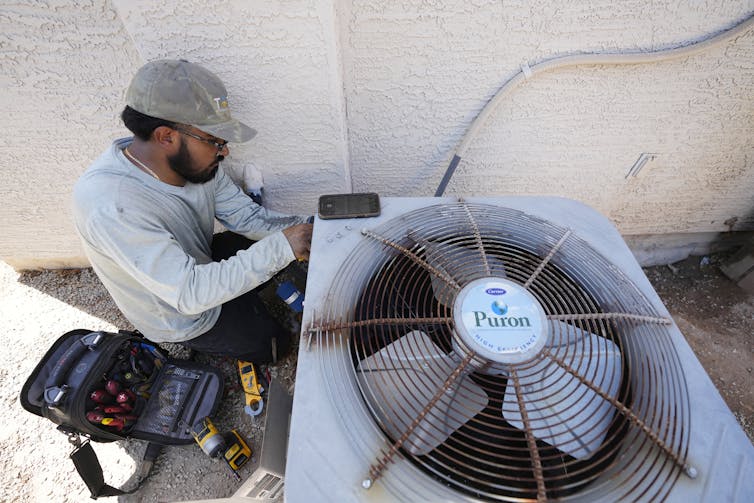 A workman fixes an air conditioning unit