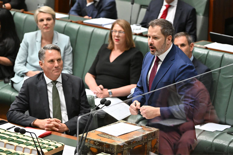 Richard Marles, seated in parliament, looks up at Ed Husic, who is giving a speech