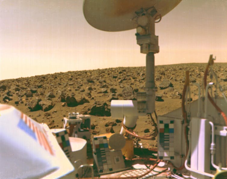 A photo showing the front of a lander as well as dusty, rocky terrain.