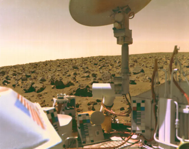 A photo showing the front of a lander as well as dusty, rocky terrain.