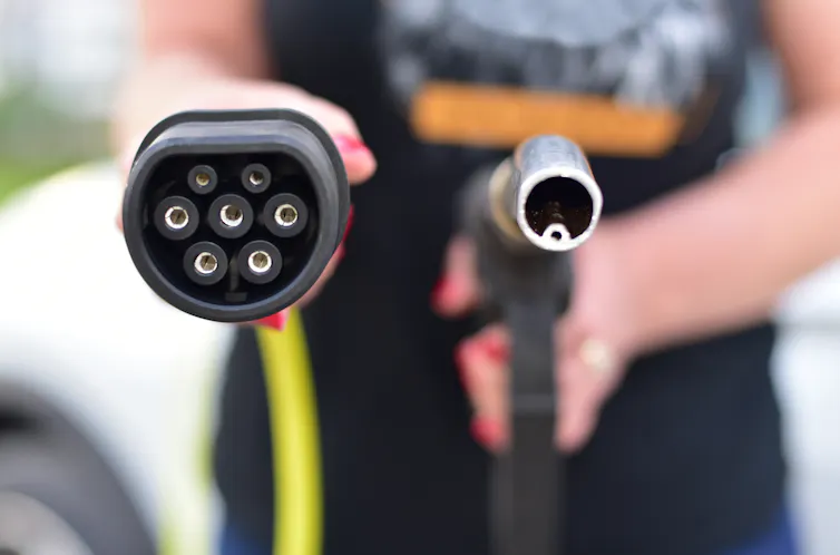 woman holding EV charger plug and fuel nozzle.