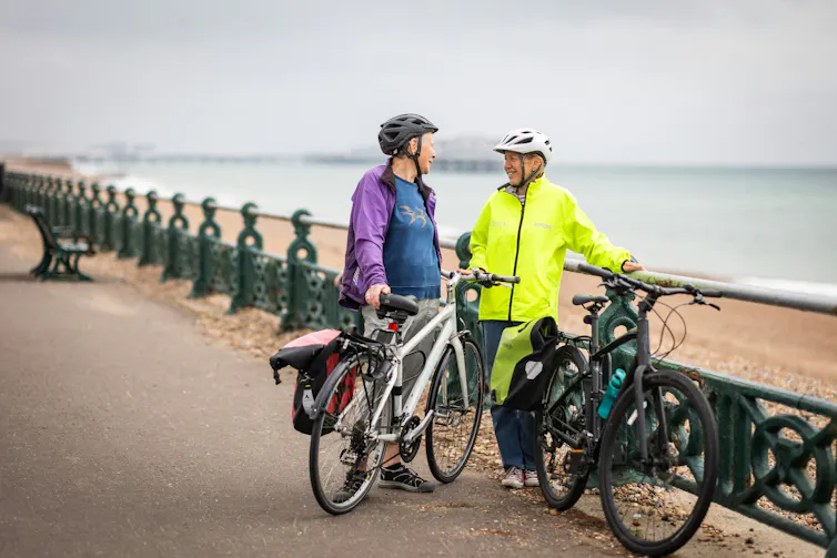 Cyclists talk, holding their bikes on a beach-front path