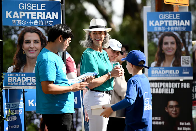 Woman in teal top and white hat surrounded by blue corflutes depicting a dark haired smiling woman