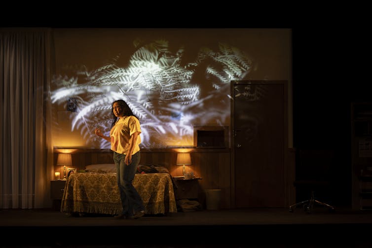 Production image: a woman in a hotel room, ferns projected on the wall.