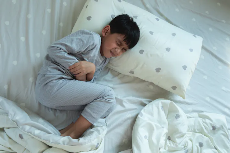 A boy lying in bed clutching his stomach.