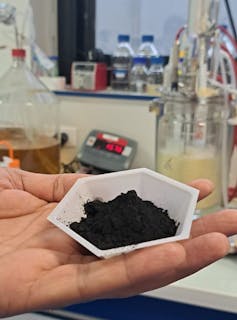 The soil, the hidden face of the air pollution by way of the PFA. And the tracks to decontaminate them 1 Photo taken in a lab with a hand holding a plastic cup containing black powder: Biochar