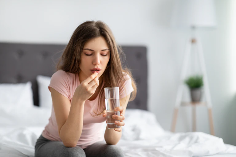 A young woman takes a pill with a glass of water.